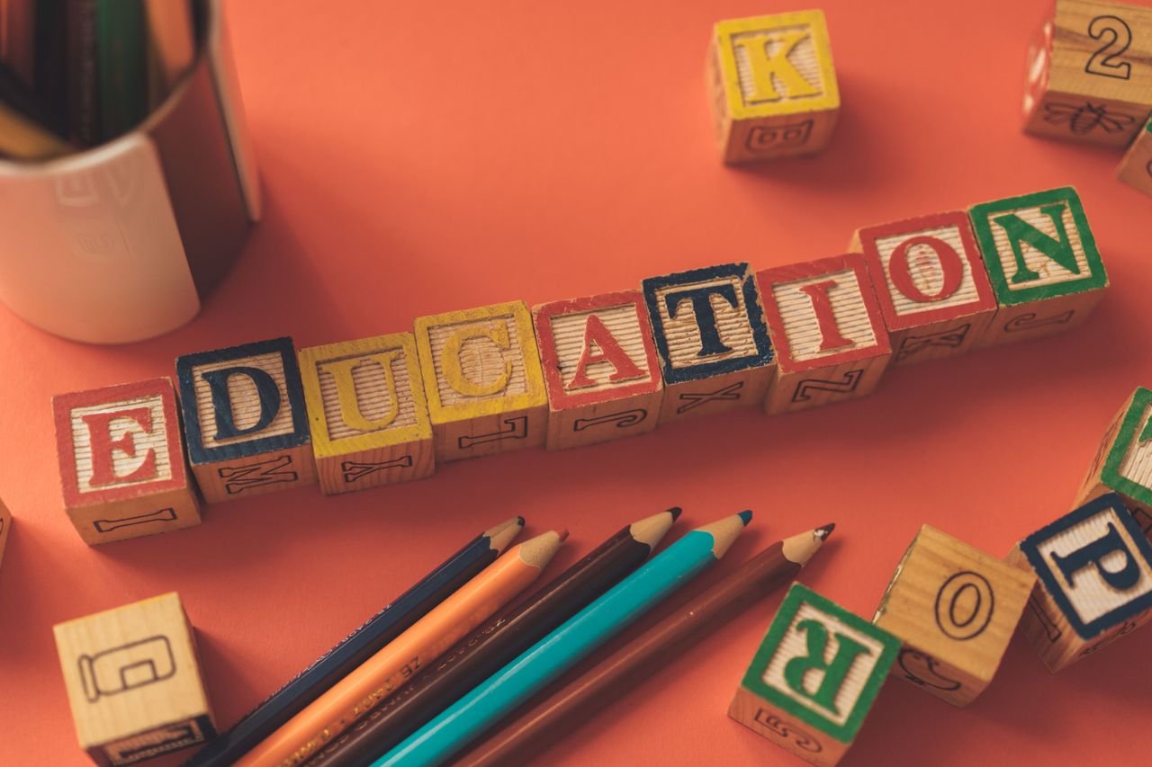 about-us-01 Alphabet blocks spelling 'EDUCATION' on orange background with pencils.
